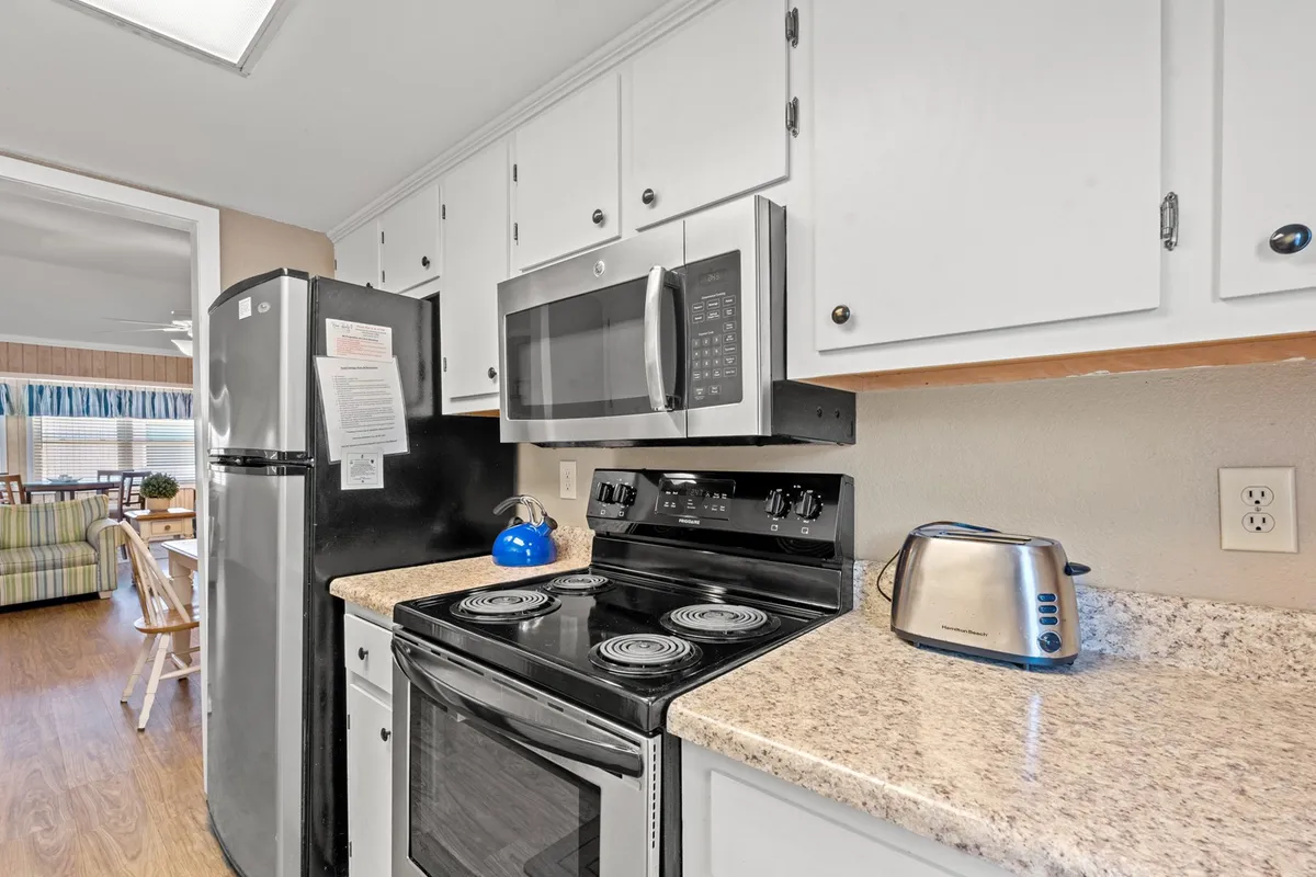 A modern, inviting kitchen featuring stainless steel appliances, a granite countertop, a stove with a blue kettle atop it, and ample space for cooking and gathering. The scene suggests a welcoming atmosphere perfect for preparing meals or enjoying morning routines.