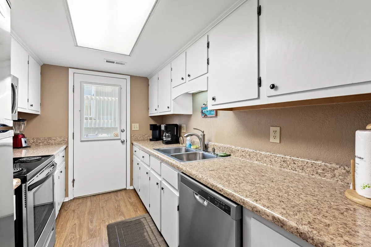 A practical kitchen view focusing on countertops, sink, various appliances, and a door leading outside. The layout emphasizes functionality for hosting gatherings or enjoying shared meals, capturing the essence of daily life and comfort in the kitchen.