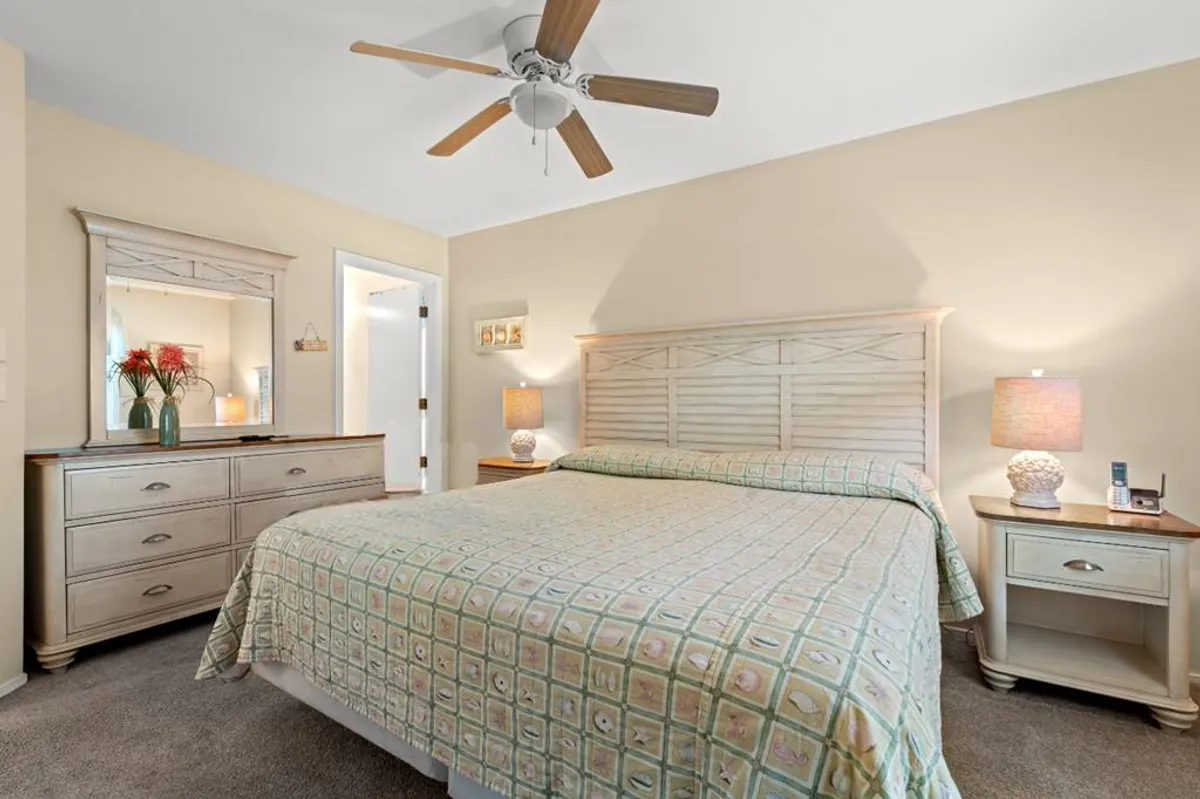 A cozy King or Queen bedroom featuring a comfortable bed with patterned bedding, wooden dresser, and nightstands with lamps. Sunlight streams through the window, filling the room with warmth and inviting relaxation.