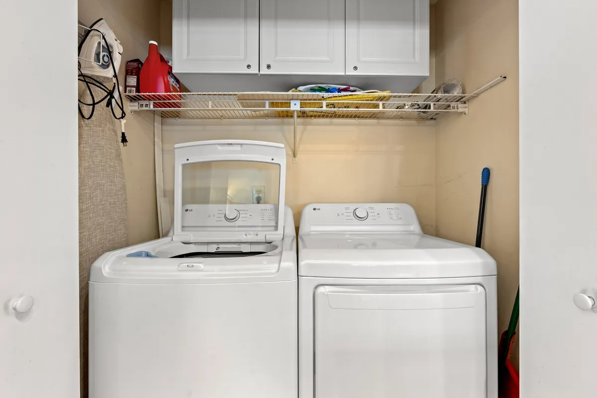 A clean, organized laundry area featuring a washing machine, dryer, and shelves stocked with laundry supplies. The arrangement conveys tidiness and convenience for guests needing quick refreshes or handling laundry during extended stays.