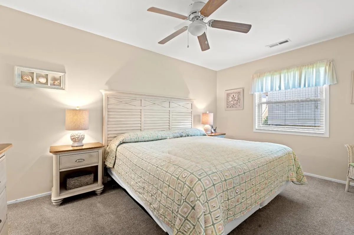 A serene bedroom featuring a comfortable bed with patterned bedding, a nightstand with a lamp, and a window adorned with light curtains letting in soft natural light. The atmosphere is calm and inviting, ideal for rest and relaxation.