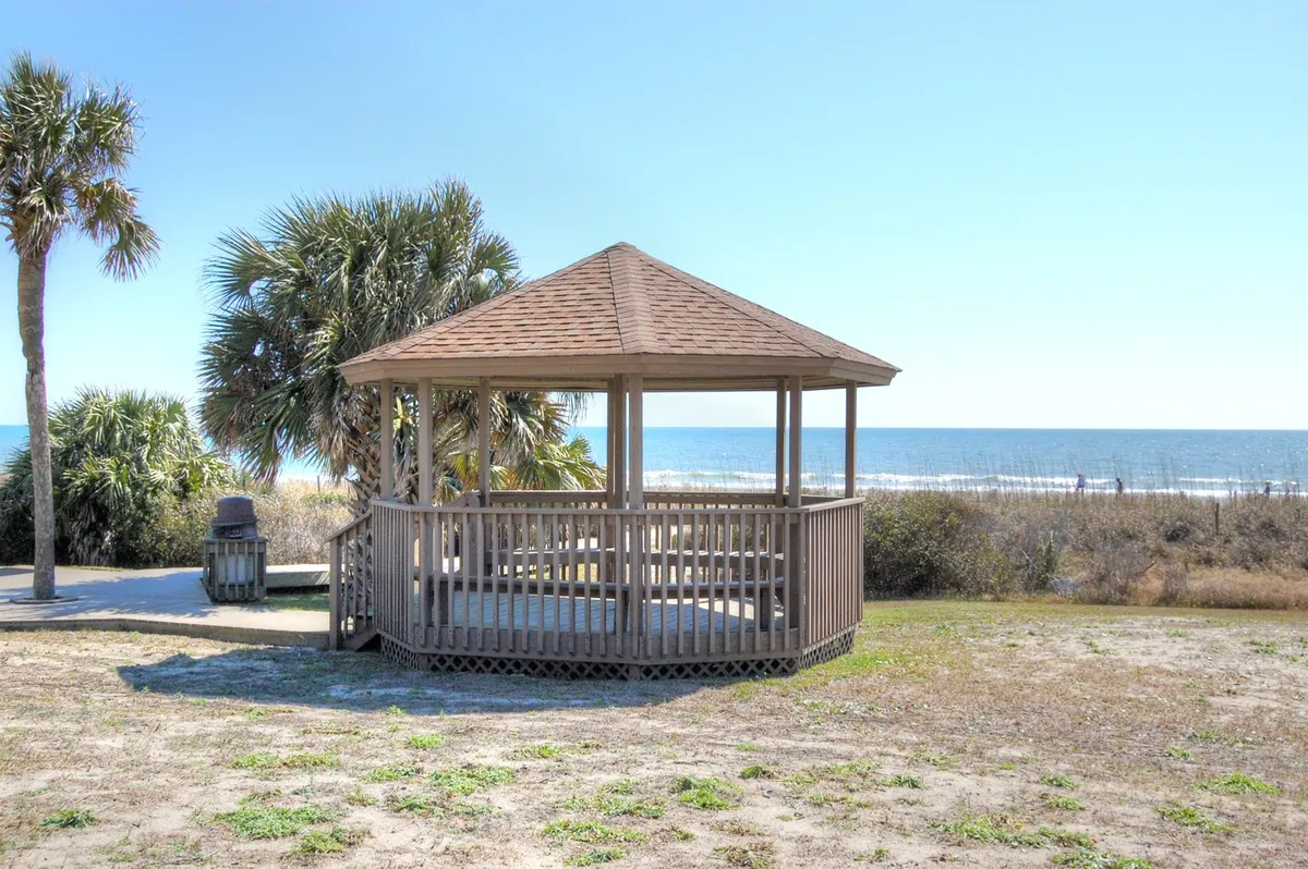 An exterior view of a charming gazebo facing the ocean, framed by palm trees. The location offers a serene spot for reading, picnicking, or simply soaking in the sea breeze and scenic views—an emblematic representation of Myrtle Beach's leisurely outdoor lifestyle.