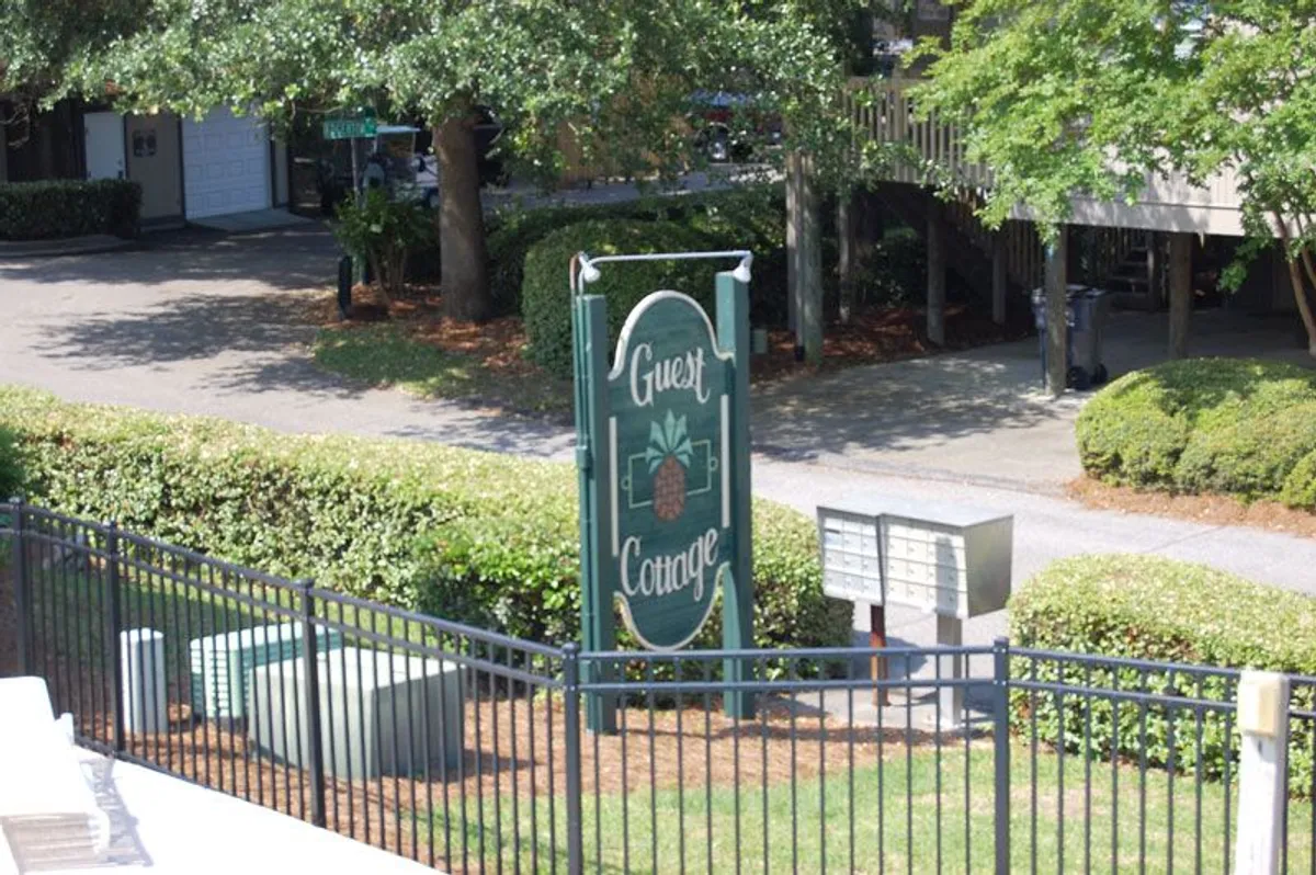 This image highlights the front area of the cottage, featuring a 'Guest Cottage' sign, well-maintained greenery, and mailboxes. The scene conveys a friendly, community-oriented atmosphere, and hints at the ease of arrival and everyday convenience for guests planning longer stays.
