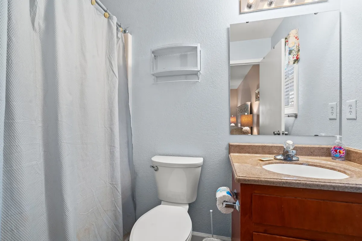 A bright, practical bathroom with a toilet, sink, mirror, and shower curtain, designed for everyday convenience and relaxation. The décor is clean and inviting, with soft lighting enhancing the soothing atmosphere.