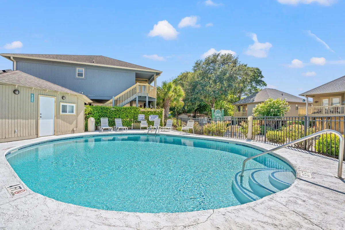A sparkling community swimming pool is surrounded by lush greenery, lounge chairs, and a building structure in the background. The pool area is shown in use, inviting guests for swims, sunbathing, and social gatherings, embodying the shared resort amenities described.