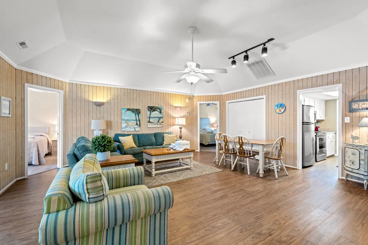 This photo captures a bright, open-concept interior featuring a striped sofa, a spacious dining table, and artwork on the wall. The dining area seamlessly connects to the living space, and the kitchen entrance is visible, suggesting easy flow between rooms. The furnishings are comfortable and inviting, with plenty of space for groups to gather, dine, and relax.