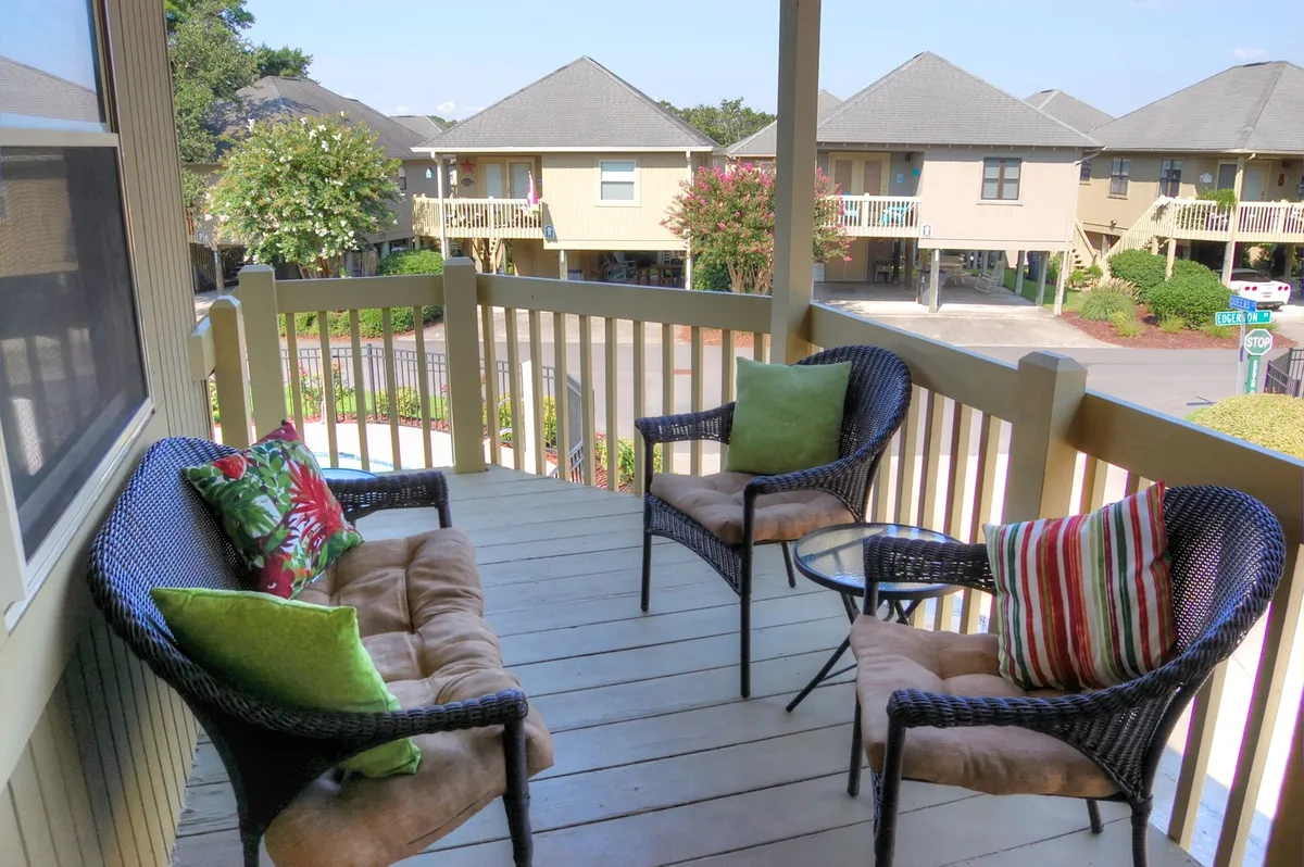 This image shows a tranquil balcony setup with wicker chairs, decorative cushions, a small table, and a view of the street. It suggests a peaceful spot for relaxing, reading, or enjoying a drink while observing the neighborhood. The setting highlights the blend of privacy and connection to the community, ideal for snowbirds or long-term guests seeking both comfort and a sense of place.