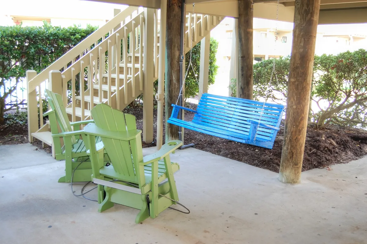 The image shows a pair of green Adirondack chairs and a blue swing set in a tranquil outdoor setting. The area is shaded and surrounded by greenery, inviting guests to relax, converse, or enjoy quiet moments together—suggesting an ideal spot for unwinding after a day of adventure.